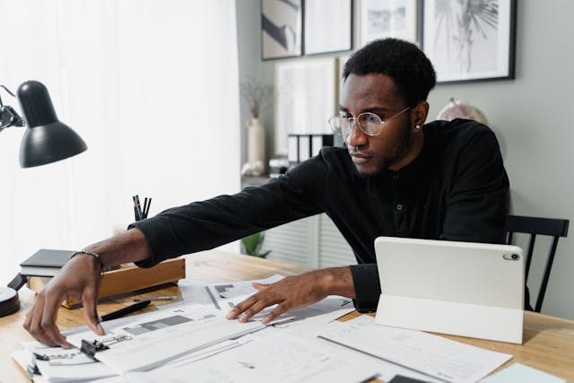Person reaching for documents across a desk with a tablet propped up in front of them